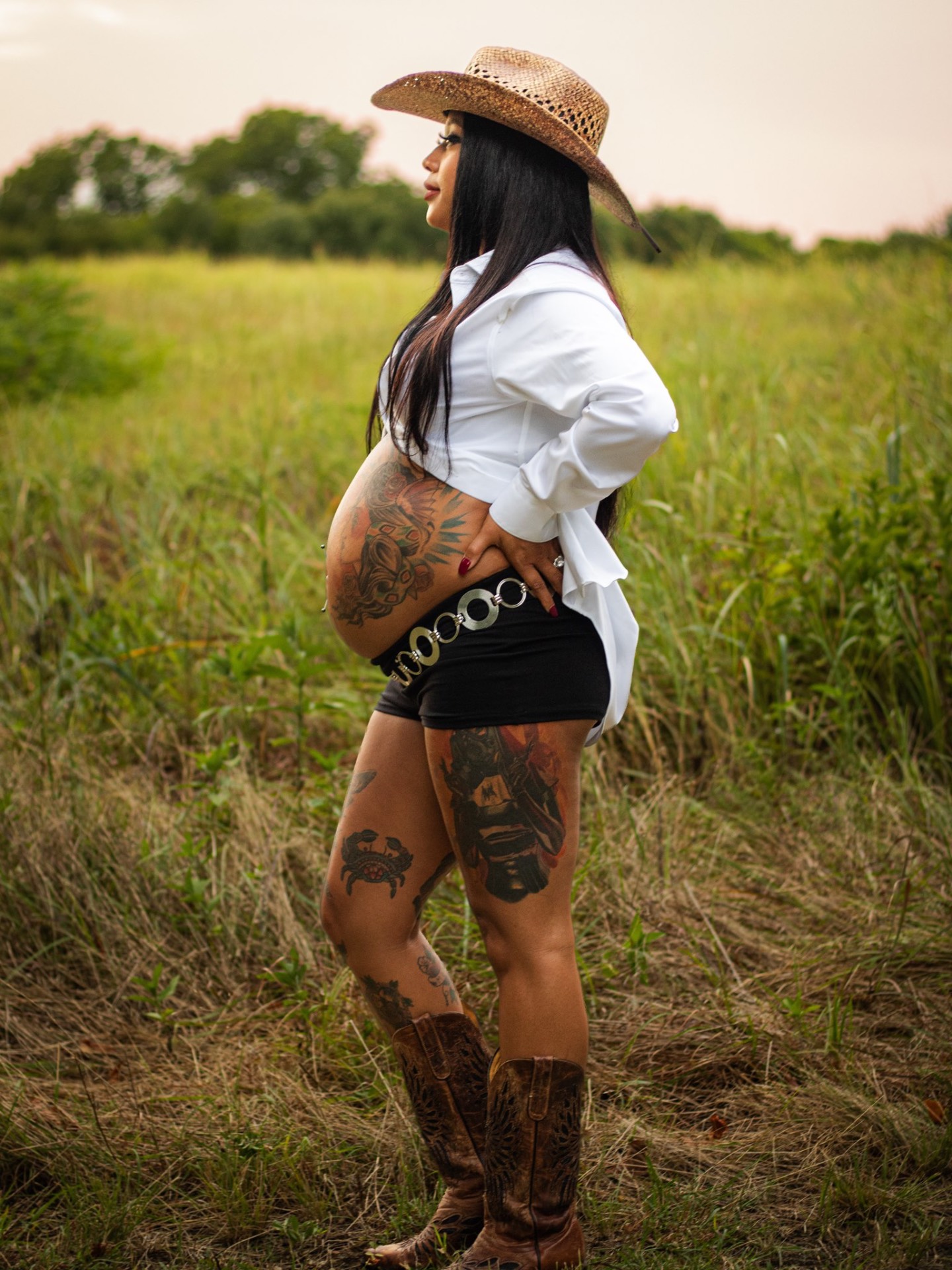 Expecting mother in a cowboy hat and boots in a Texas field at sunset