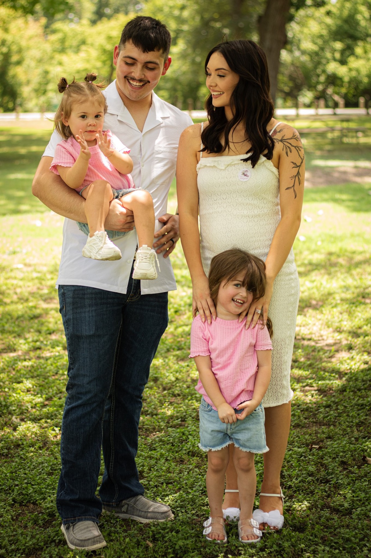 Expecting family of four smiling together in a sunny park