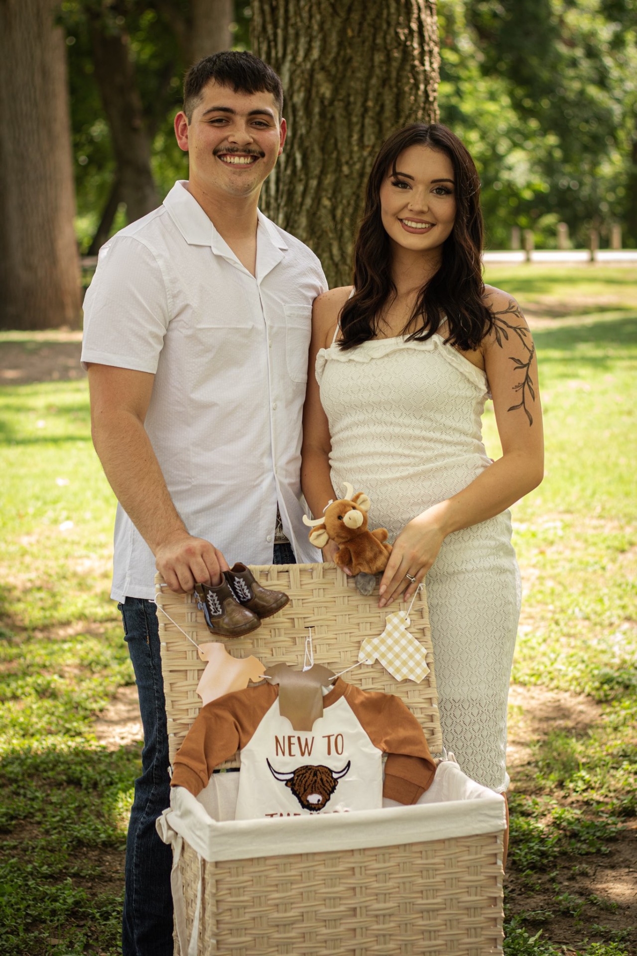 Expecting couple with a western-themed baby announcement basket under an oak