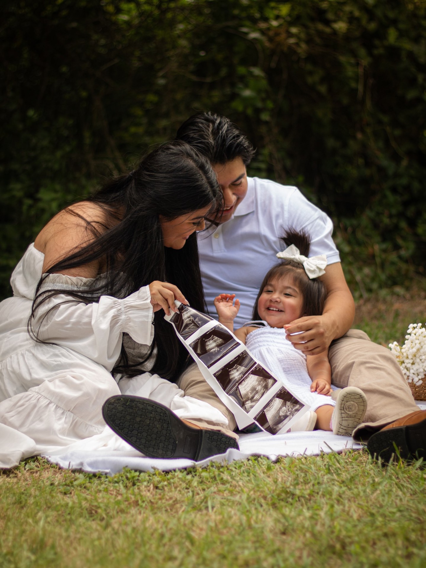 Family sitting on a blanket showing a sonogram to their little girl