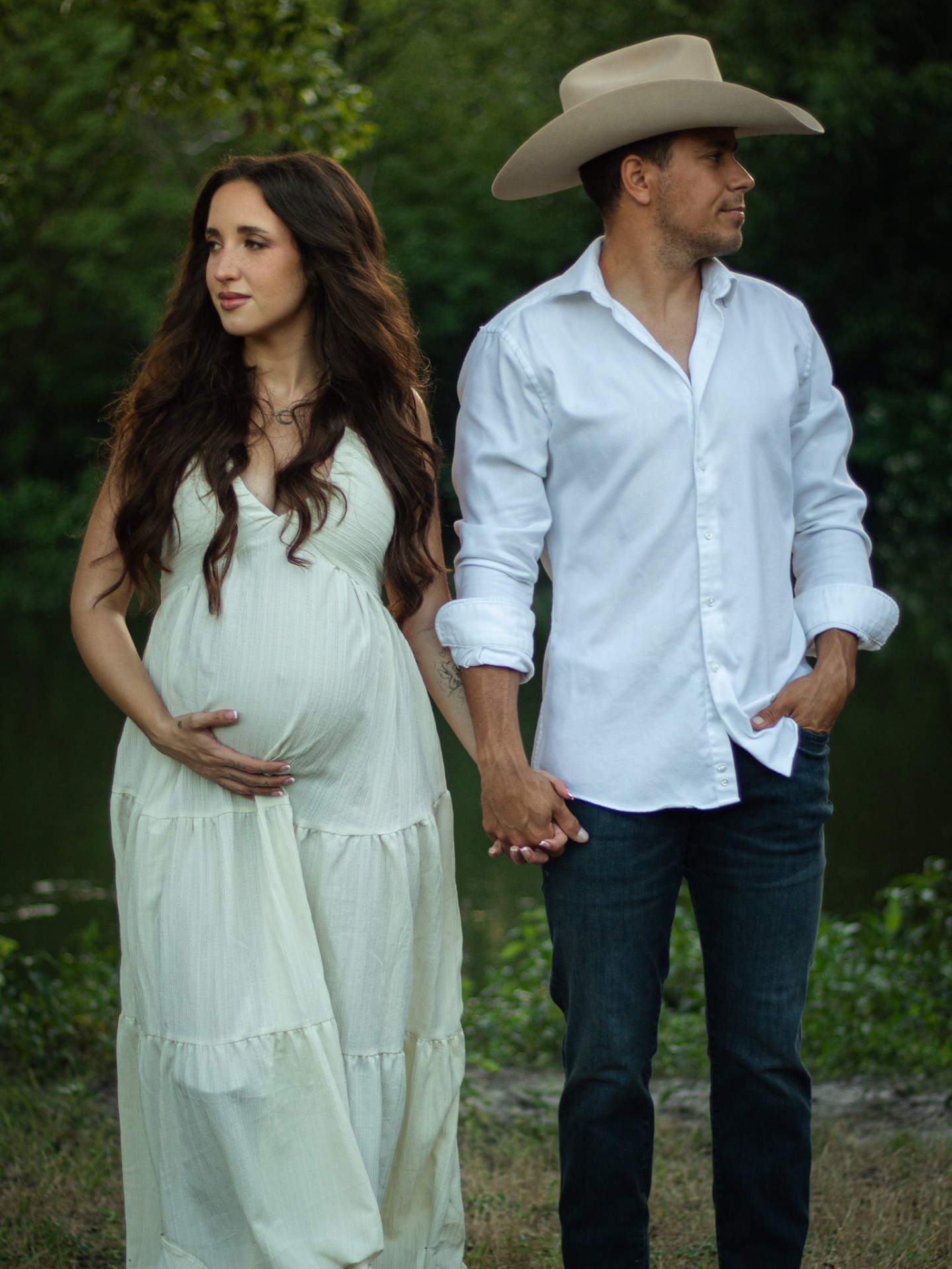 Expecting couple holding hands by a Texas creek at dusk